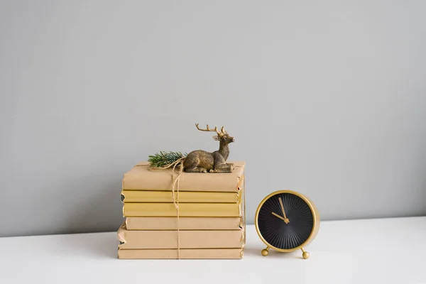 Pile of books in craft covers on a white shelf, souvenir deer and table clock