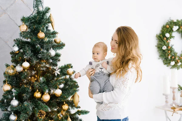 A young mother with blonde hair holds her little son in her arms, they are happily celebrating Christmas and new year