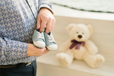 Müstakbel baba, bebek için mavi spor ayakkabıları tutuyor. Oğlunun gelecekteki çocuğundan hoş ve ürpertici bir beklenti..