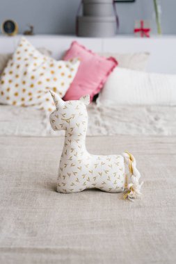 Soft unicorn toy on the bed with pillows in the bedroom bedding colors clipart