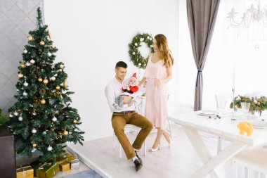 Noel Baba kostümlü mutlu ve genç bir aile Noel 'i kutluyor ve Noel ağacıyla birlikte oturma odasında kutluyor.
