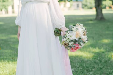 Şık ve güzel düğün buketi, yeşil çimlerin arkasında gelinin elinde.