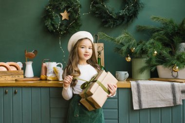 Bir kız, elinde yılbaşı ve yeni yıl için süslenmiş zümrüt saten bir kurdeleyle Noel hediyesi tutuyor. Açılış hediyesi
