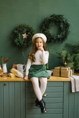 Bere takmış şık bir kız mutfakta oturuyor, Noel ve yeni yıl için süslenmiş ve baget yiyor.
