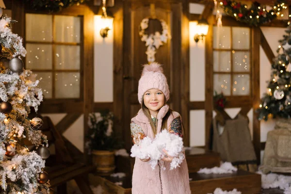 Девушка Розовой Шляпе Жилете Держит Искусственный Снег Фоне Заснеженного Дома — стоковое фото
