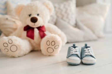 Küçük çocukların mavi spor ayakkabıları yastıkların ve yumuşak oyuncakların arka planına karşı masanın üzerinde yatıyor. Yeni doğmuş bir bebeği bekleme konsepti.