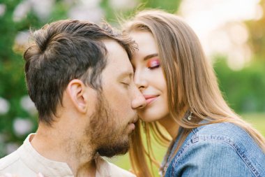 Birbirine aşık mutlu genç bir çift, gülümsüyor ve yaz parkında yürüyüş yapıyor. Romantizm ve dinlenme kavramı. Sevecen bir şekilde onun yanaklarını arıyor ve kız arkadaşı karnında kelebekler hissediyor.