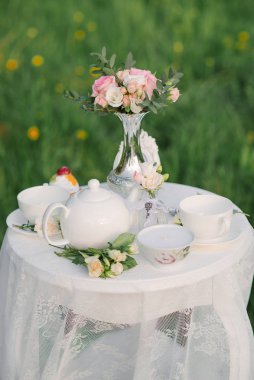 Çay servisi, bir buket gül ve gümüş bir vazoda, sehpanın üzerinde dantel masa örtüsü olan bir vazo. Düğün dekoru, romantik bir akşam için dekor.