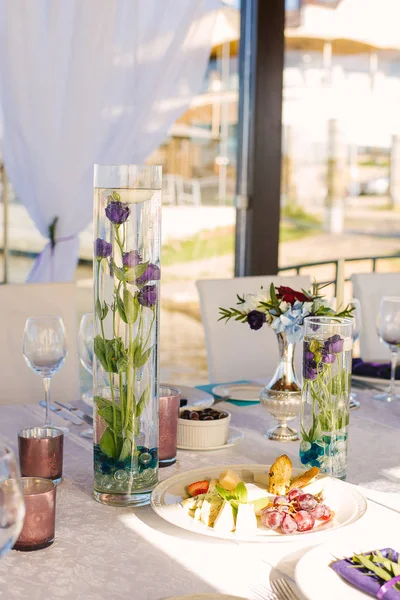Wedding decor. Purple eustoma flowers are submerged in glass vases flasks on the festive table
