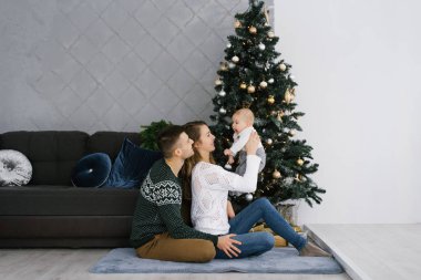 Genç ve mutlu bir aile ve küçük bir oğlu oturma odasındaki Noel ağacının yanında oturuyorlar.