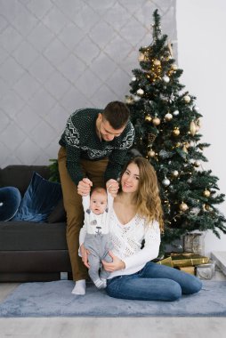 Genç bir oğlu olan mutlu bir aile oturma odasındaki bir Noel ağacının yanında yerde oturuyor. Mutlu yıllar ve tatiller.