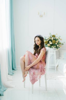 Pembe elbiseli güzel bir esmer gelin, bacaklarını altına sıkıştırmış bir sandalyede, klasik bir aydınlık yatak odasında oturuyor..
