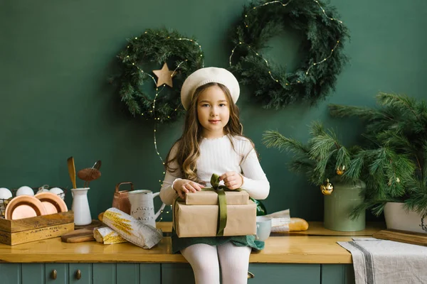 Beyaz bereli şirin bir kız elinde Noel hediyeleri ve zümrüt renkli mutfakta oturuyor. Yeni yıl tatili için süslenmiş.