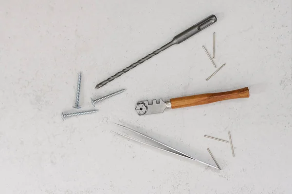 Construction tools: glass cutter with wooden handle, drill for puncher, tweezers, nails and screws on a light background