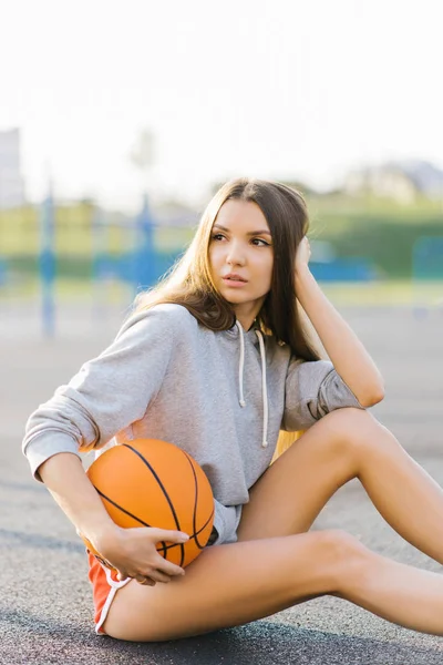 Dívka Basketbalista Sedí Hřišti Drží Míč Rukou Dívá Jinam — Stock fotografie
