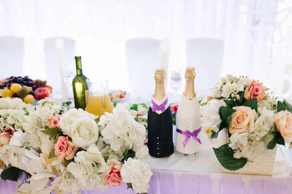 Twee flessen champagne, verkleed als bruid en bruidegom, stonden in bloemen op de feesttafel — Stockfoto