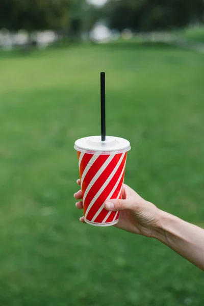 Une tasse en papier à rayures rouges et blanches avec un tube en plastique. boissons à emporter à la main. Une main de femme tient une tasse en papier sur un fond — Photo