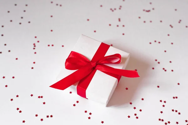 White gift box with red satin ribbon on white background with co