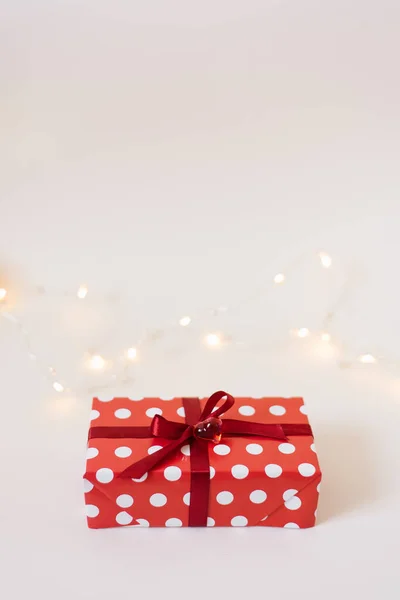 Gift box in red paper packaging with white polka dots, tied with — Stock Photo, Image