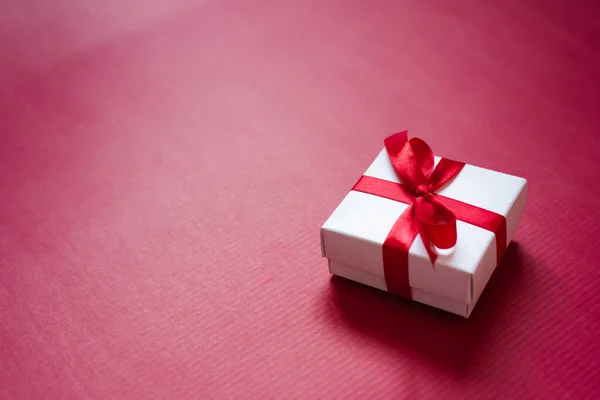 Saten kurdeleli beyaz hediye kutusu ve kırmızı bir kağıt üzerinde yay — Stok fotoğraf