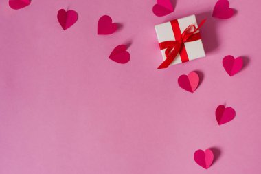 Kağıt pembe kalpler ve kırmızı saten kurdeleli bir hediye kutusu.