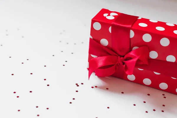 Geschenk verpakt in rood papier met witte cirkels en een rode satijnen strik — Stockfoto