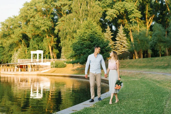 Um jovem casal apaixonado caminha ao longo da margem de um lago em uma cidade — Fotografia de Stock