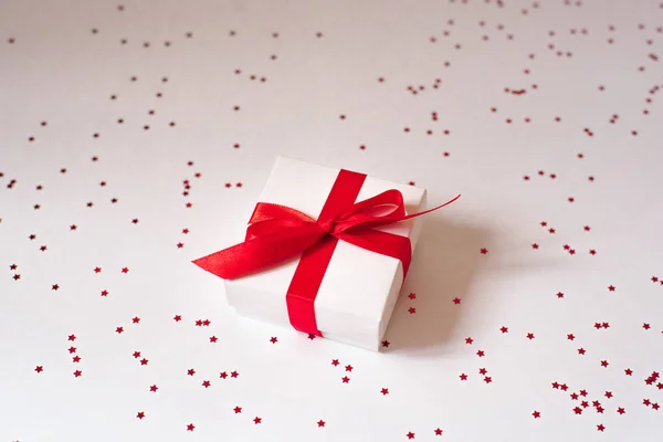 Kırmızı kurdeleli bir hediye ve beyaz arka planda bir yay ve kırmızı bir c — Stok fotoğraf