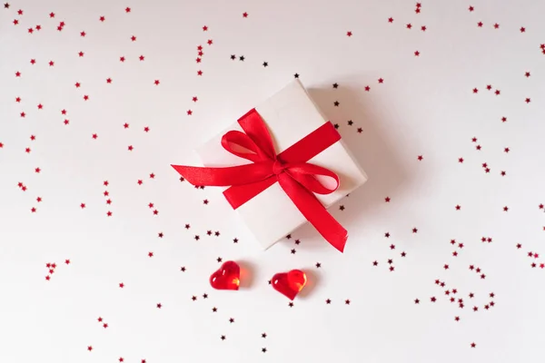 Un regalo con una cinta roja y lazo sobre un fondo blanco y dos —  Fotos de Stock