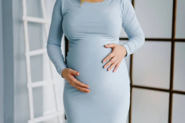 A woman holds her hands on her pregnant belly in a blue dress. W — 스톡 사진