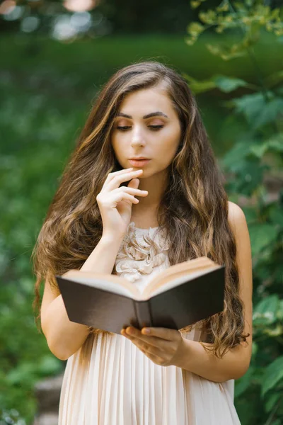 Romantic long haired young beautiful woman holding a book and re — Stock Photo, Image