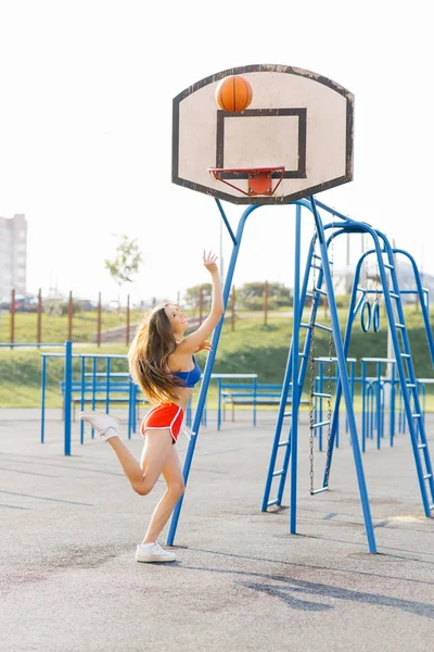 Piękna wysportowana szczupła dziewczyna rzuca koszykówkę do R — Zdjęcie stockowe