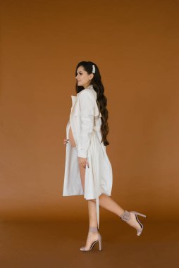 Stylish pregnant woman in underwear and light raincoat on a brow