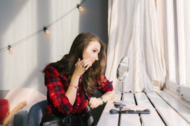 Kız makyajını evde yapıyor ve masaüstü masasına bakıyor. 
