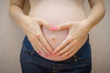 Bir kadın bir kalp ve bir çift eli çıplak hamile olarak tutuyor. 