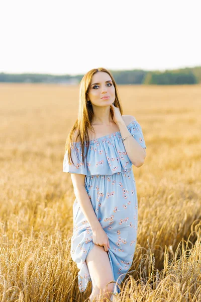 A pregnant young woman in a blue sundress stands in a field of w