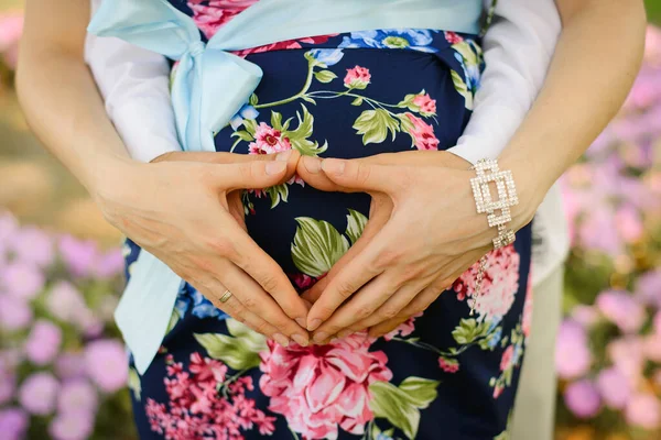 Ein Herz aus den Händen eines Ehepaares auf schwangerem Bauch — Stockfoto