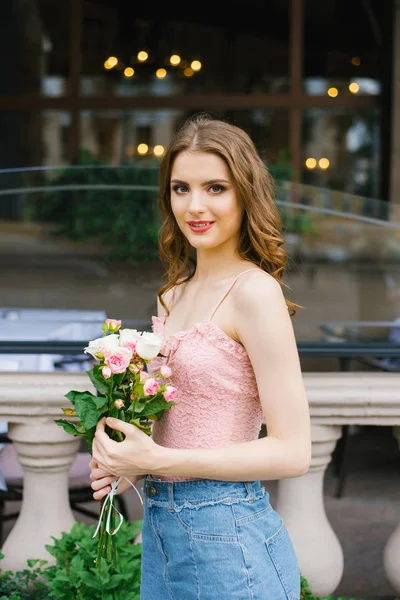Una hermosa joven caucásica sosteniendo un ramo de rosas y — Foto de Stock