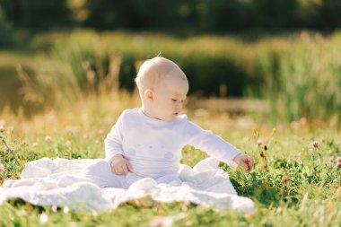 Küçük bir çocuk açık havada gölün kıyısındaki bir battaniyeye oturur. Bebeğinle yaz yürüyüşleri.
