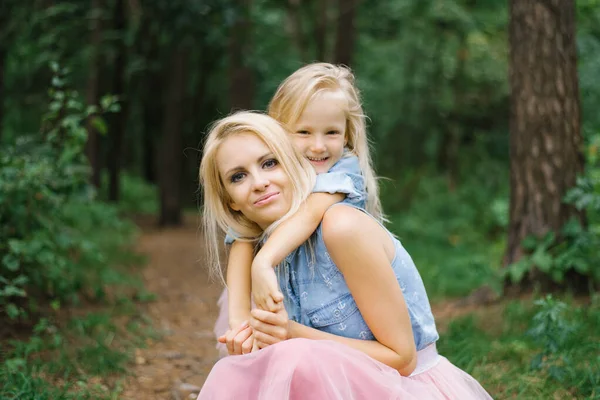 A mother and a five-year-old daughter in identical pink tulle skirts and blue denim shirts are walking in the Park or in the woods. The daughter hugs her mother. Mother's day