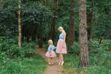 Aynı romantik kıyafetleri giyen bir anne ve beş yaşındaki kızı parkta ya da ormanda yürüyorlar. Mutlu çocukluk ve annelik