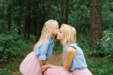 Aynı romantik kıyafetleri giyen bir anne ve beş yaşındaki kızı parkta ya da ormanda yürüyorlar. Kızım annemi yanağından öpüyor.