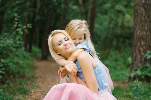 A mother and a five-year-old daughter in identical pink tulle skirts and blue denim shirts are walking in the Park or in the woods. The daughter hugs her mother. Mother\'s day