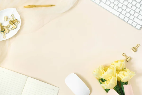 スタイリッシュな女性用デスク オフィスデスク コンピューター 黄色のチューリップの花束 クリップボードとのワークスペース ライトベージュの背景に女性のファッションアクセサリー 平面上面 — ストック写真