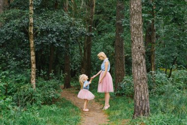 Aynı romantik kıyafetleri giyen bir anne ve beş yaşındaki kızı parkta ya da ormanda yürüyorlar. Mutlu çocukluk ve annelik