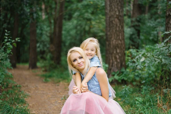 A mother and a five-year-old daughter in identical pink tulle skirts and blue denim shirts are walking in the Park or in the woods. The daughter hugs her mother. Mother\'s day