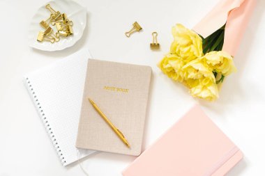 Spring Feminine çalışma alanı blogcusu. Kalemli defterler, beyaz arka planda sarı laleler. Moda tarzı düz yatak