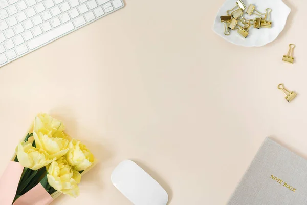 Flat lay blogger or freelancer workspace with Notepad, keyboard and a bouquet of yellow peony tulips