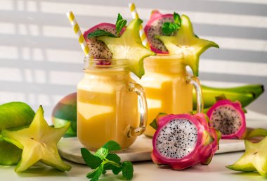 Güneşli bir pencerenin yanında içilmeye hazır iki tropikal egzotik meyve suyu..