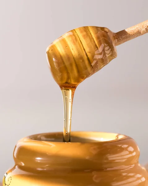 Uma vista de perto de um mergulhador de mel pingando com mel em um pote de mel . — Fotografia de Stock